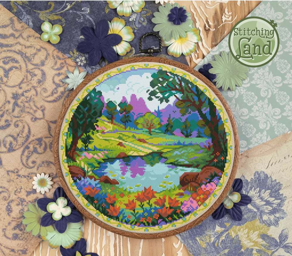 Bright stamped cross-stitched landscape in an embroidery hoop with decorative flowers and 'Stitching Land' branding.