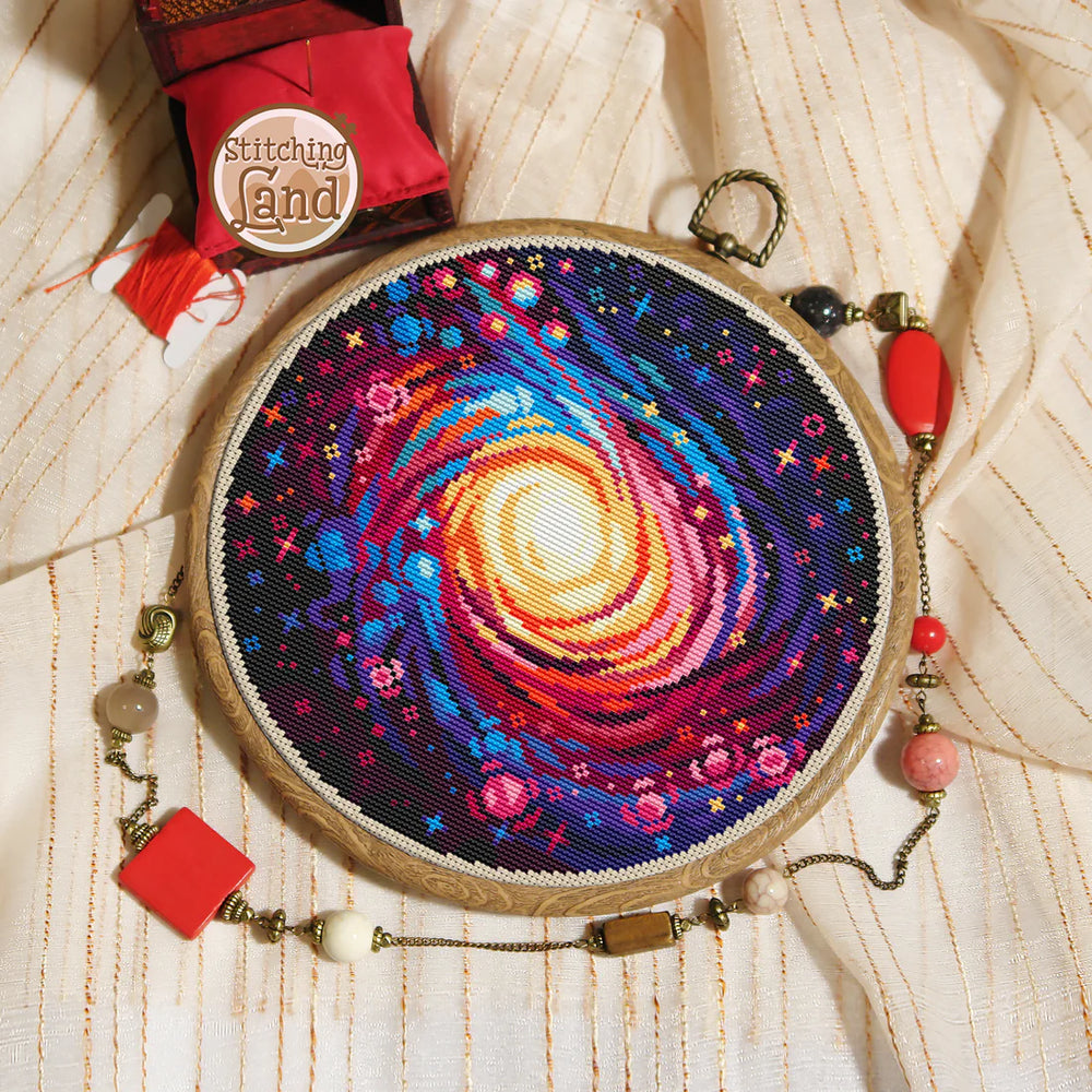 Stamped cross stitch mockup showing a Embroidery hoop with a colorful spiral design on a textured fabric background, featuring 'Stitching Land' brand.