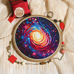 Stamped cross stitch mockup showing a Embroidery hoop with a colorful spiral design on a textured fabric background, featuring 'Stitching Land' brand.
