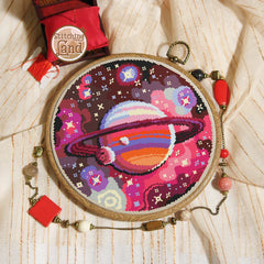 Stamped cross stitch mockup showing a Embroidery hoop with a colorful space-themed design on a textured fabric background