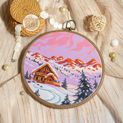Stamped cross stitch mockup showing a Embroidery hoop with a winter landscape design on a textured surface with embroidery supplies.