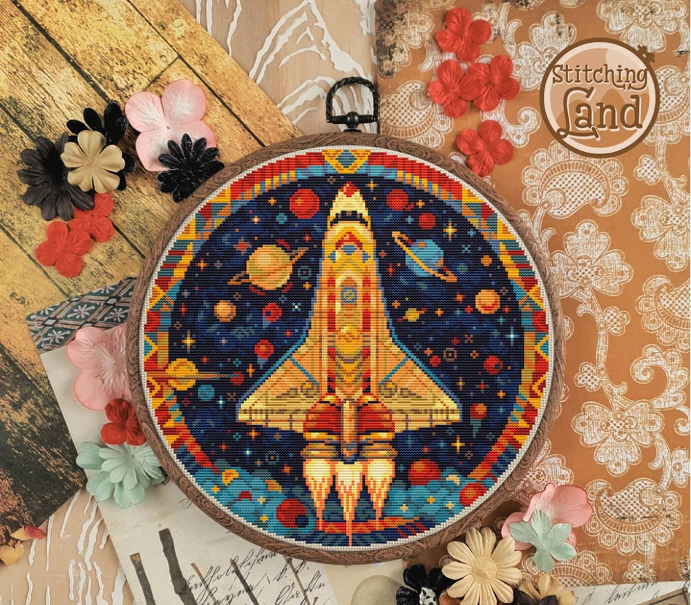 Embroidery hoop with a colourful space shuttle stamped cross stitch design on a decorative background with flowers and lace.