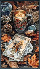 Stamped cross stitch design of  a candle, mug, cards, cinnamon sticks, and autumn leaves on a wooden surface.