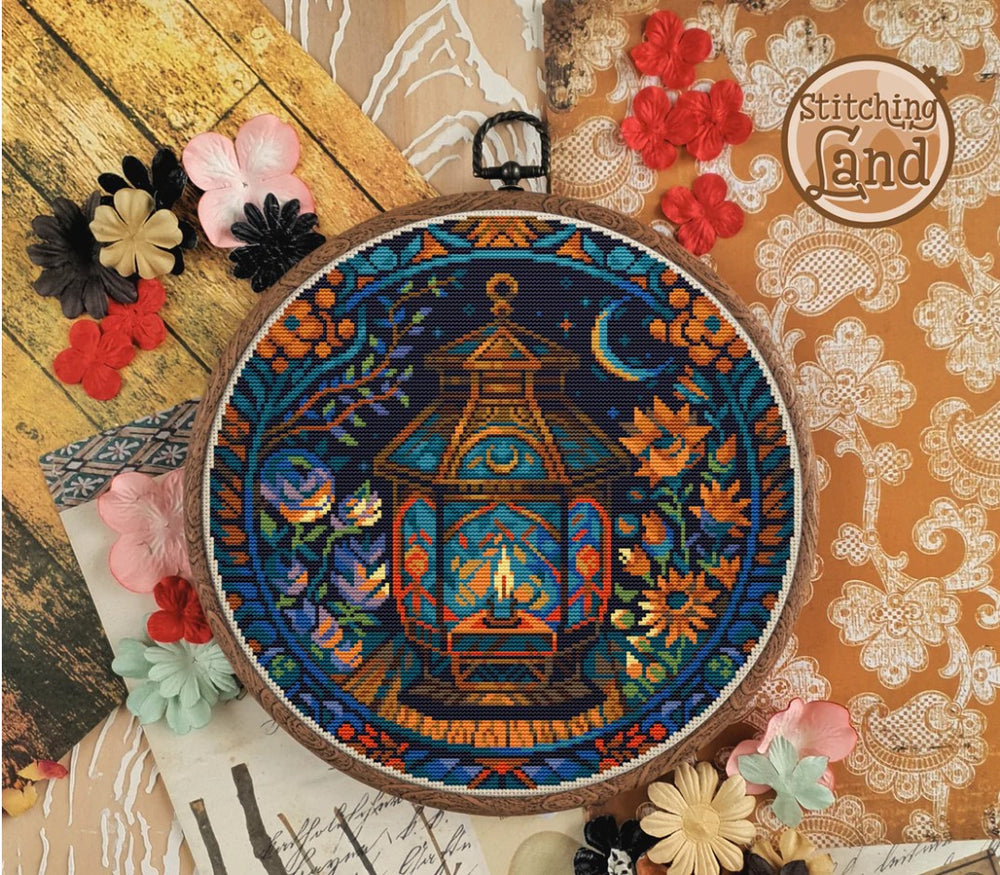 Embroidery hoop with a colorful stamped cross stitch design of a lantern and flowers on a decorative background.