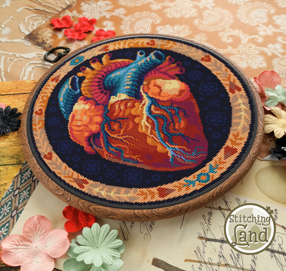 Embroidered heart design on a wooden hoop with flowers and lace in the background, brand 'Stitching Land' visible.