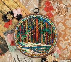 Stamped cross stitch design of a Embroidery hoop with a colorful forest design surrounded by decorative flowers and lace on a wooden surface.